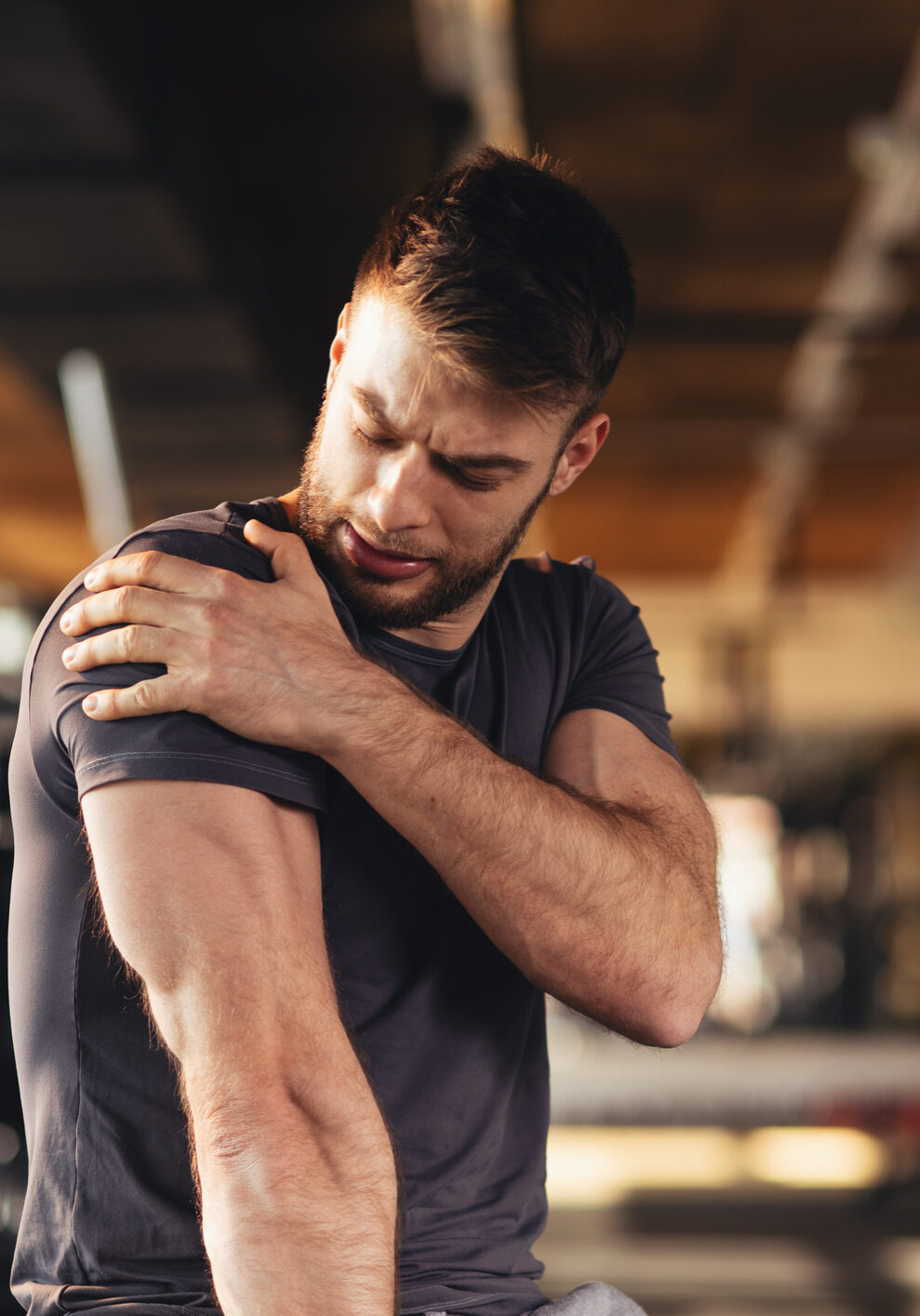 Handsome young man feeling the pain in shoulder at the gym